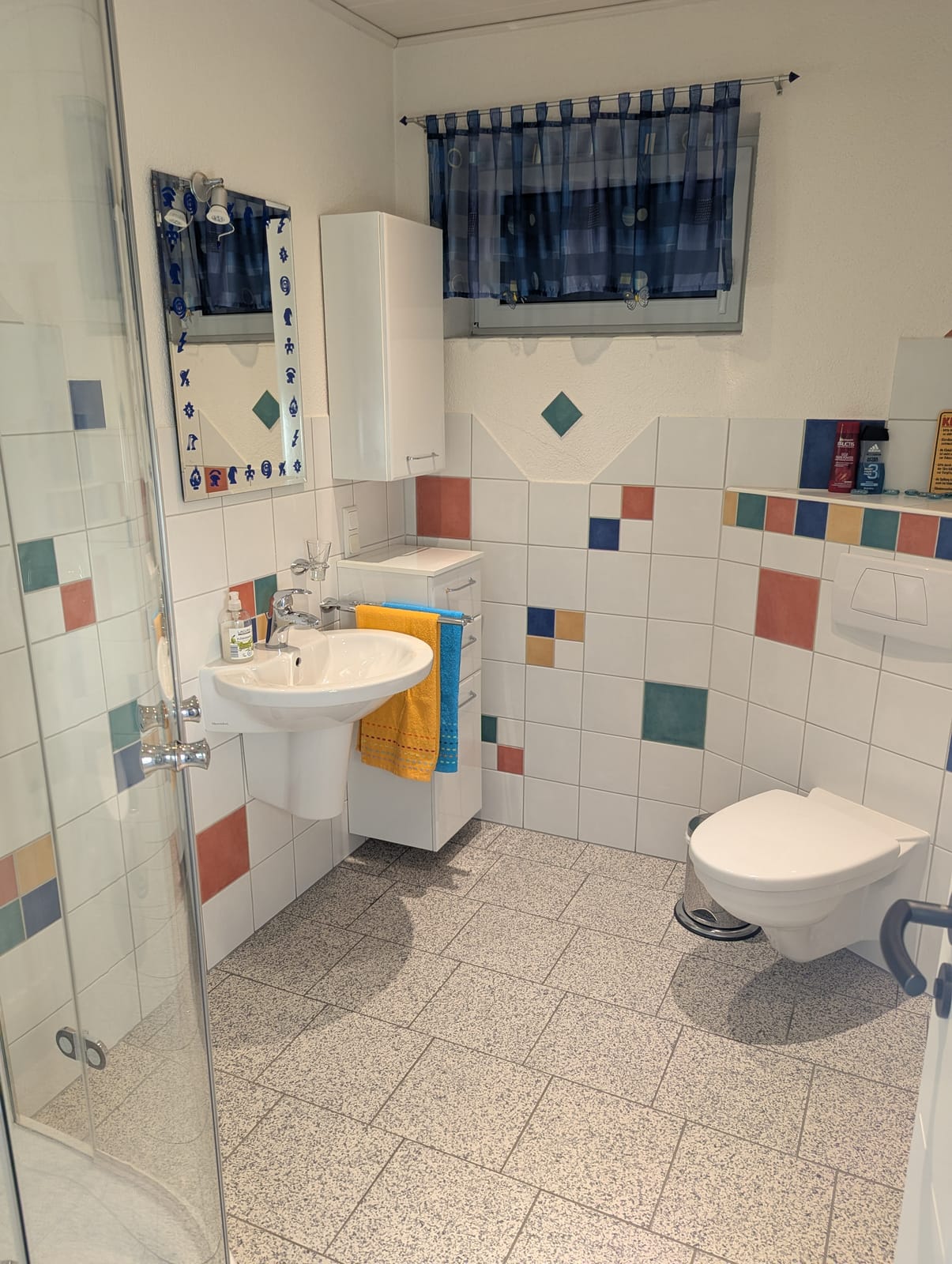 Badezimmer mit Eckdusche, Waschbecken und WC, hell gefliest mit bunten Akzenten